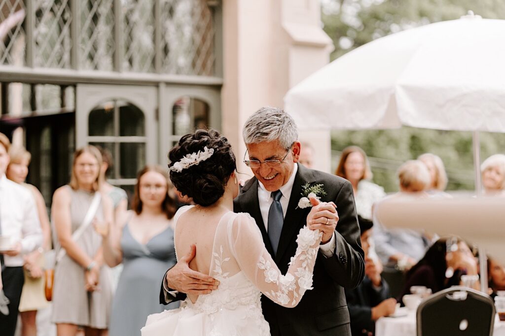 During an outdoor wedding reception at the Fowler House Mansion a father smiles as he shares a first dance with his daughter on her wedding day