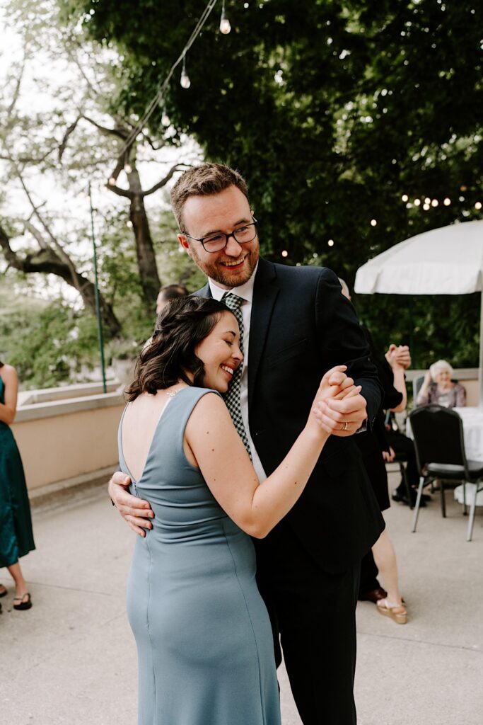 A couple smile while dancing with one another during an outdoor wedding reception
