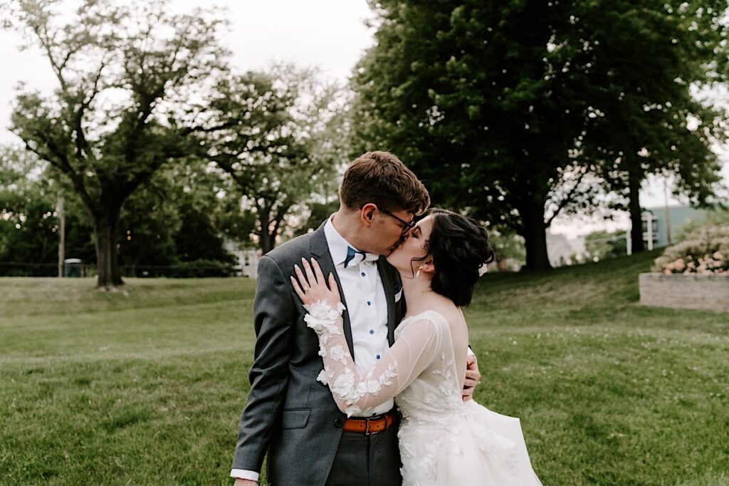 In a field outside their wedding venue the Fowler House Mansion, a bride and groom embrace and kiss one another