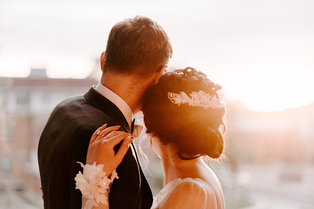 During their outdoor wedding reception at the Fowler House Mansion, a bride and groom embrace while looking away from the camera at the sunset