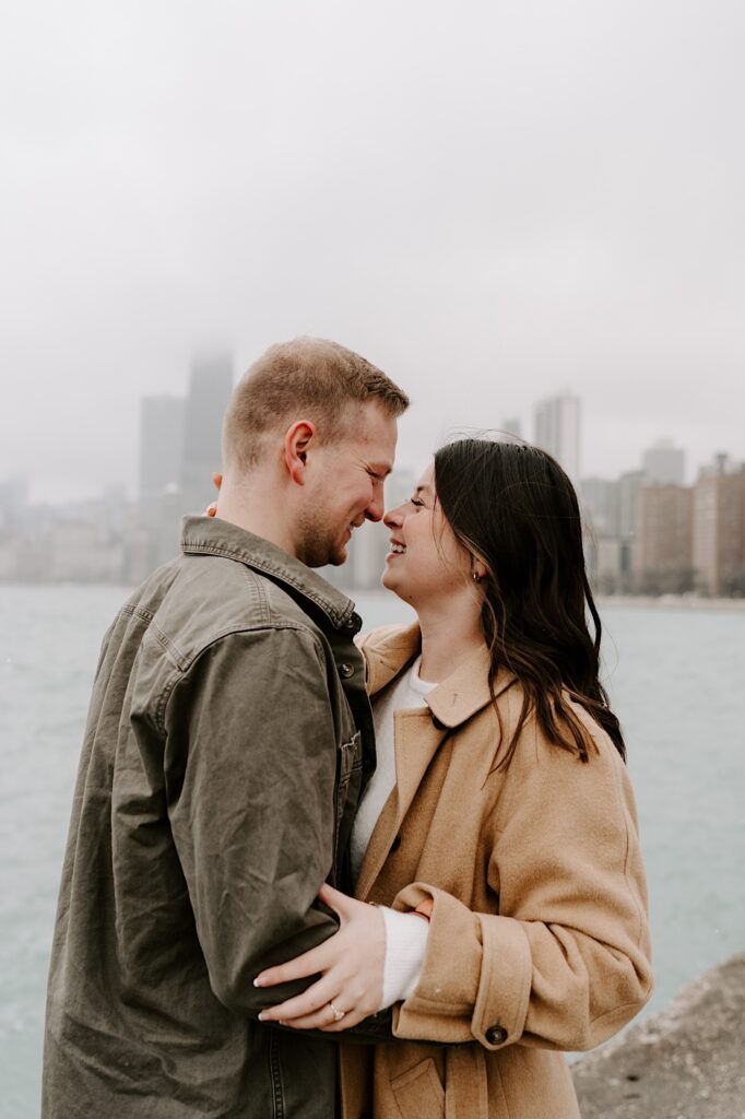 A man and woman embrace and smile at one another while standing in front of Lake Michigan and the Chicago skyline