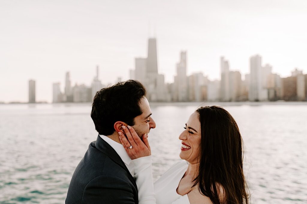A bride and groom at North Avenue Beach smile at one another during sunset with the Chicago skyline behind them