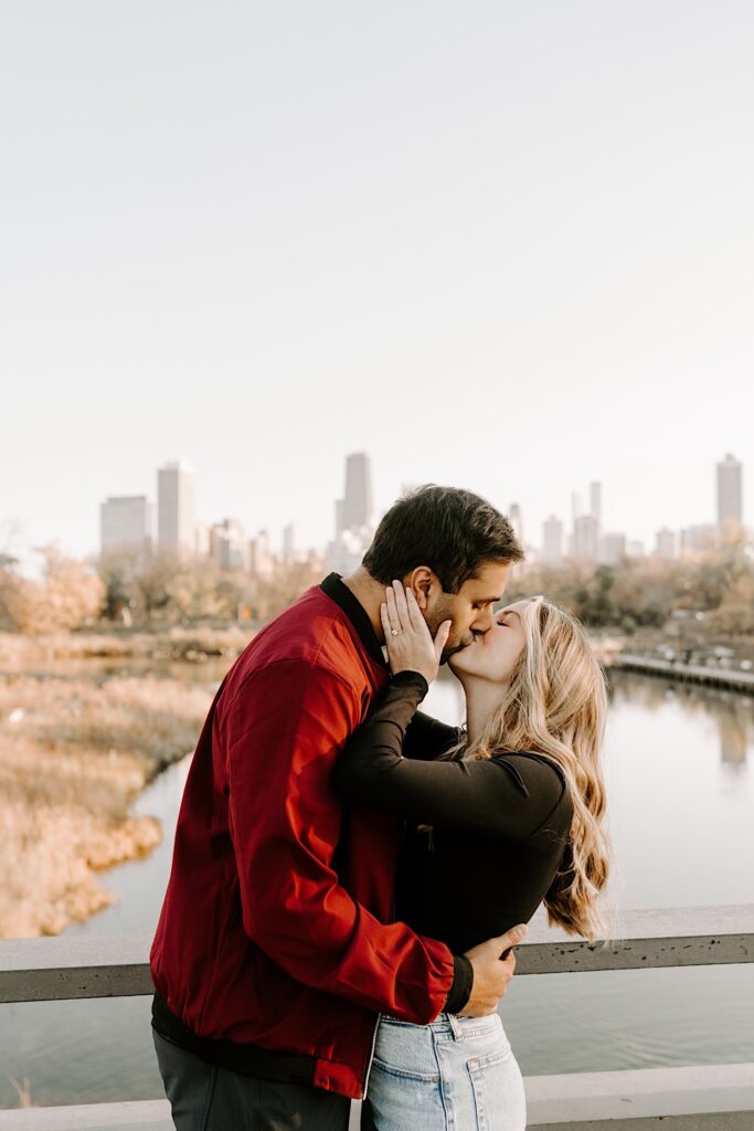 A man woman kiss one another in Chicago's Lincoln Park during the fall with the skyline and a body of water behind them
