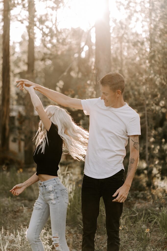 A man and woman dance with one another in the middle of a forest as the sun sets behind them
