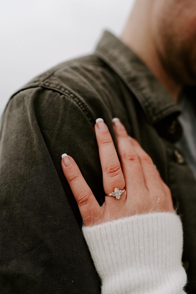 Close up photo of a woman's hand with an engagement ring resting on a man's shoulder
