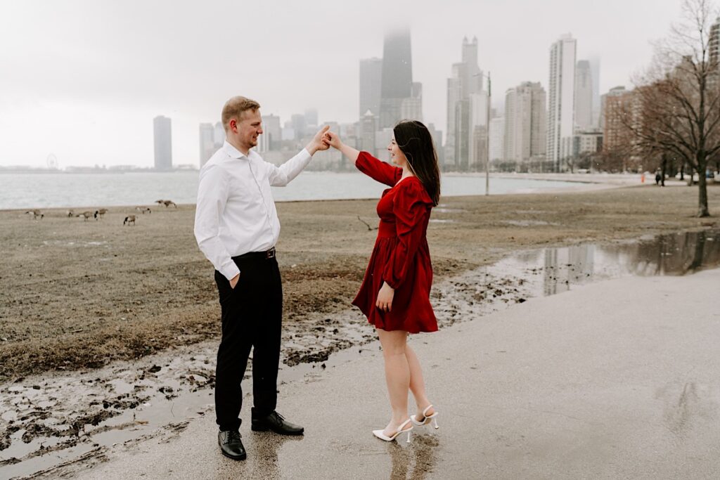 A man and woman dance in a park near North Avenue Beach during their fall engagement session with Lake Michigan and the Chicago skyline behind them