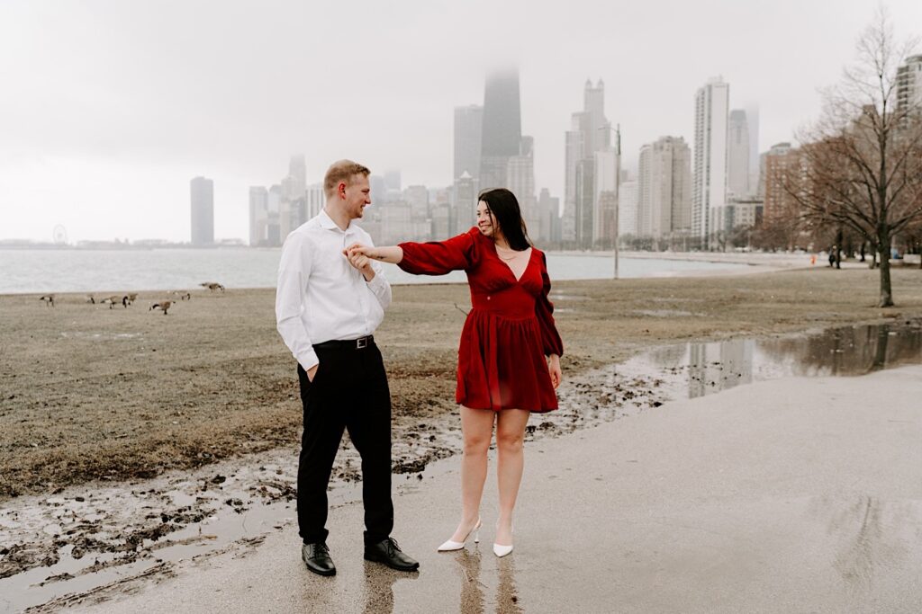 A man and woman dance in a park near North Avenue Beach during their fall engagement session with Lake Michigan and the Chicago skyline behind them