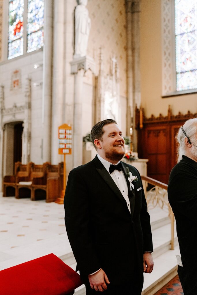 A groom smiles while standing at the altar waiting for the bride to walk down the aisle for their wedding ceremony