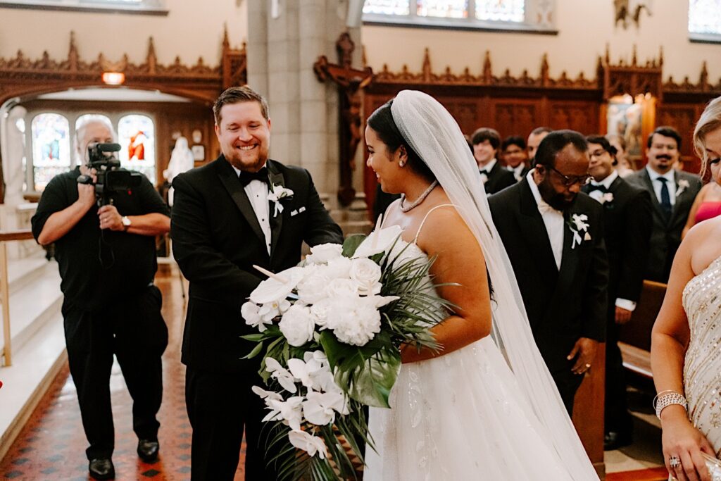 A bride and groom smile after the bride walks down the aisle and reaches the groom during their wedding ceremony in a church