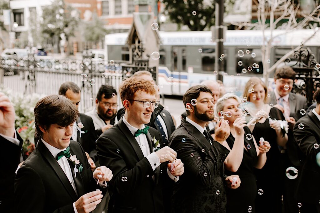 members of a wedding smile while standing outside as they blow bubbles for the newlyweds