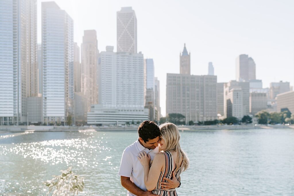 A couple embrace and smile with one another during their engagement photos, behind them is Lake Michigan and the Chicago skyline