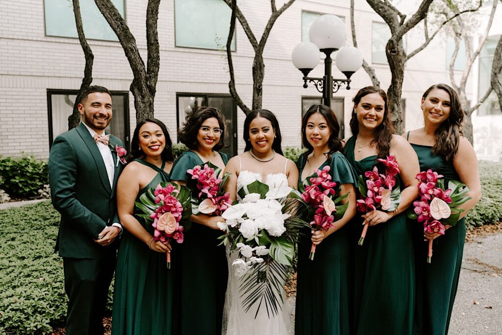 A bride stands with the 6 members of her wedding party in a courtyard as they all smile at the camera