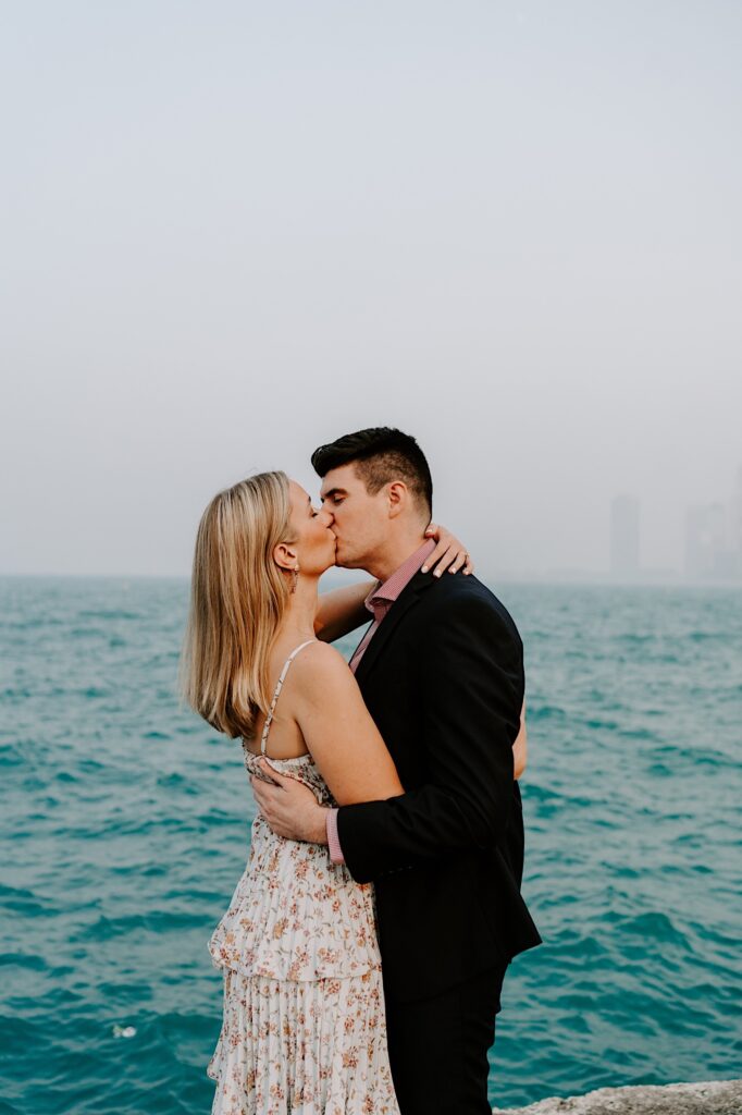 A couple embrace one another and kiss while standing in front of a lake