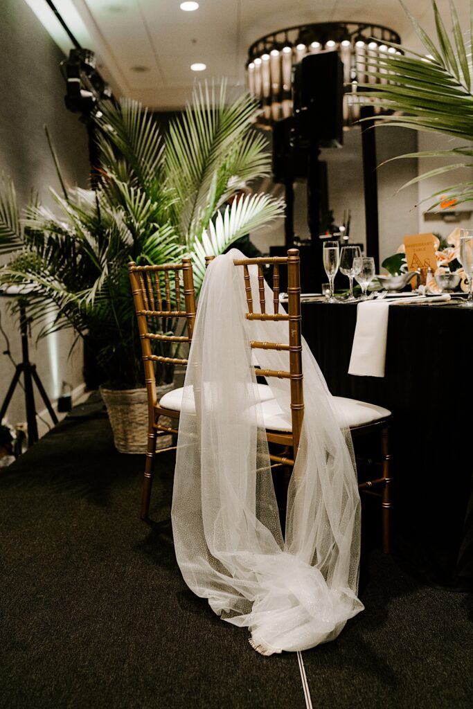 A wedding veil is draped over a chair that is seated at a table decorated for a wedding reception