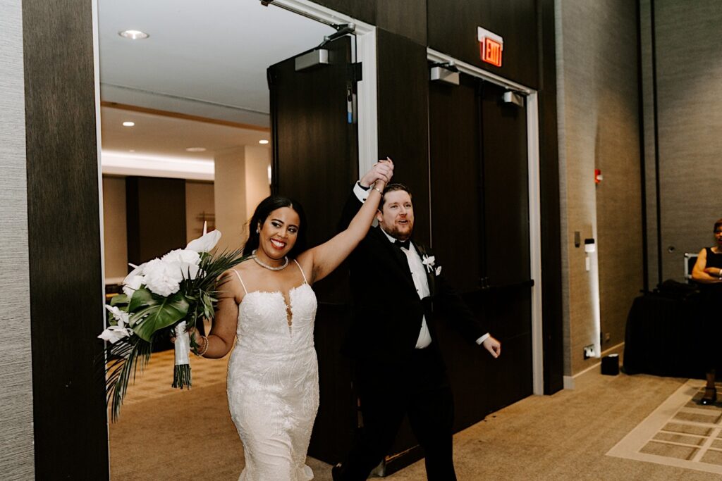 A bride and groom smile and lift their hands in the air as they enter their wedding reception at the Hyatt Regency together