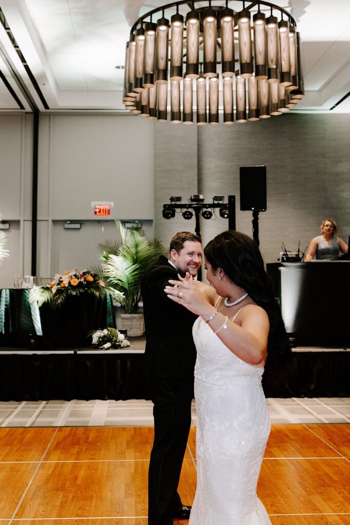 A groom smiles while he and the bride perform a dance move during their indoor wedding reception