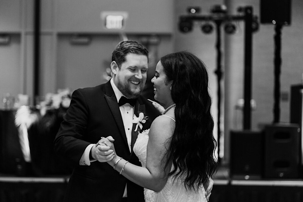 Black and white photo of a bride and groom dancing together and smiling during their indoor wedding reception at the Hyatt Regency