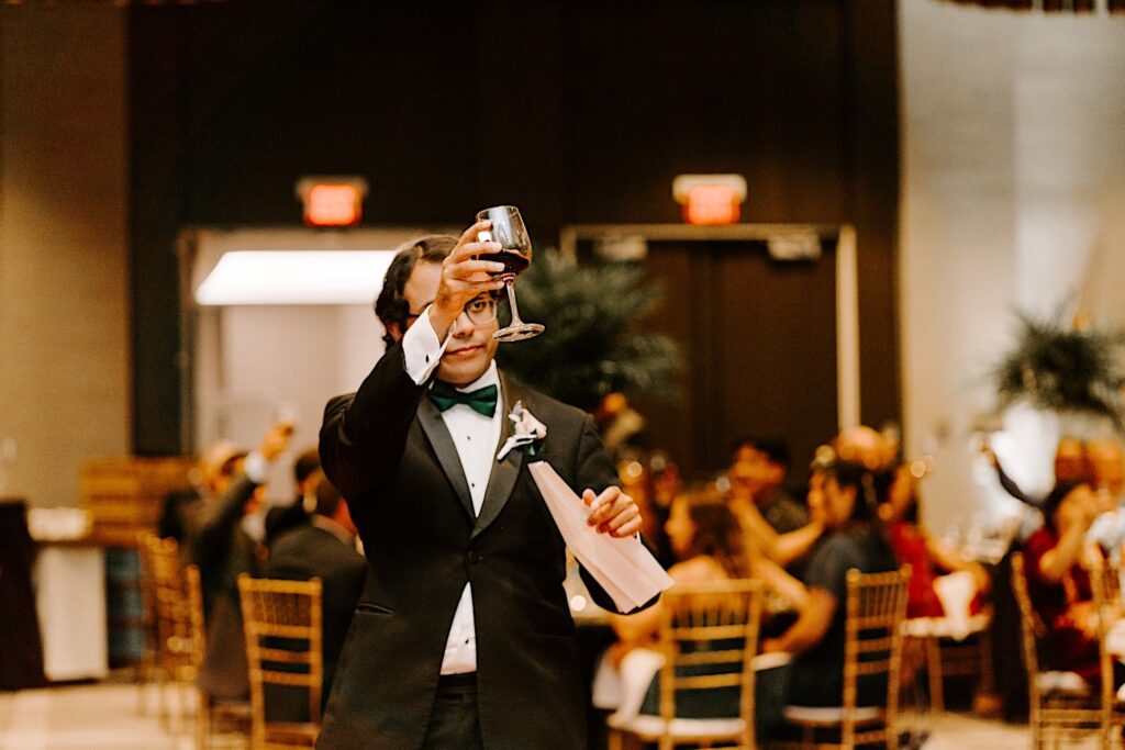 A groomsman lifts a glass as a toast after giving his speech during an indoor wedding reception at the Hyatt Regency
