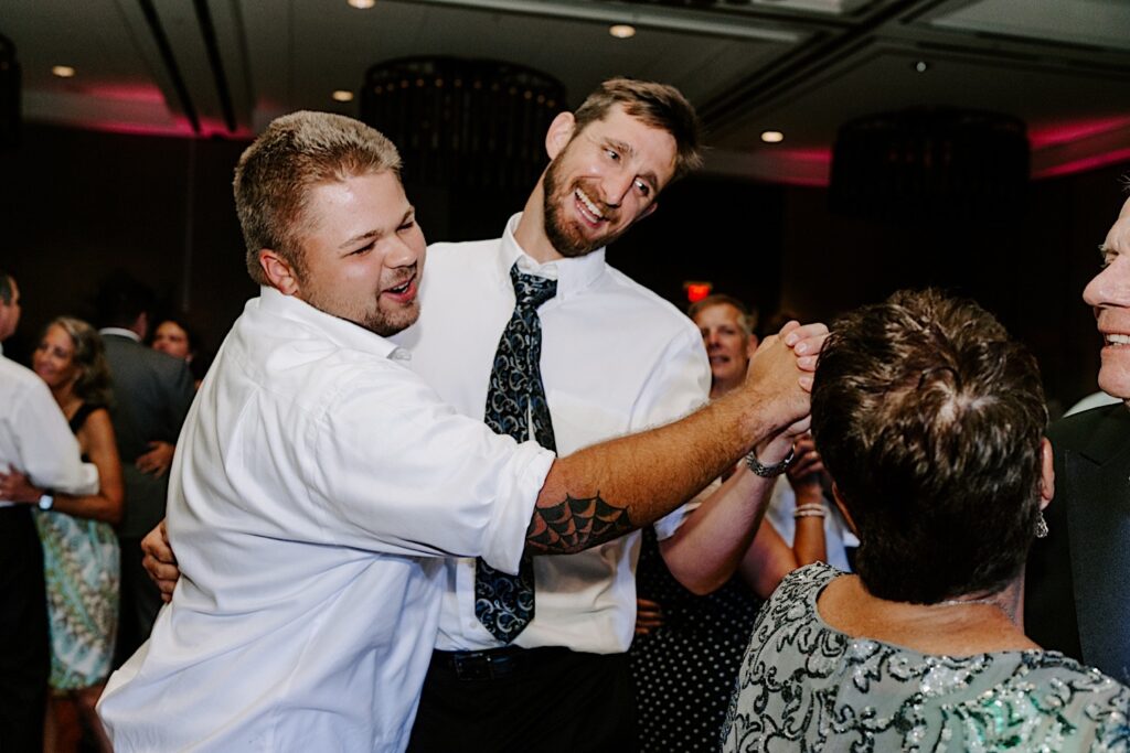 Two male guests of an indoor wedding reception at the Hyatt Regency dance together and smile towards other guests