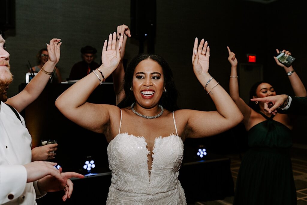 A bride smiles and lifts her arms in the air while dancing with guests of her indoor wedding reception at the Hyatt Regency