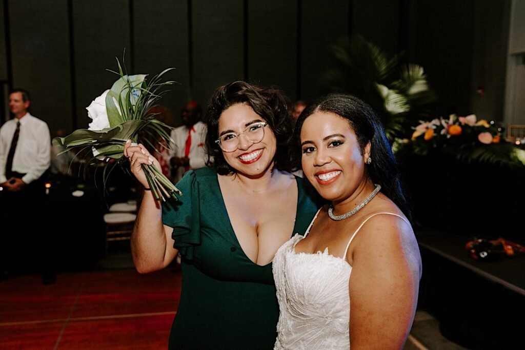 A bride and one of her bridesmaids smile at the camera during an indoor wedding reception at the Hyatt Regency