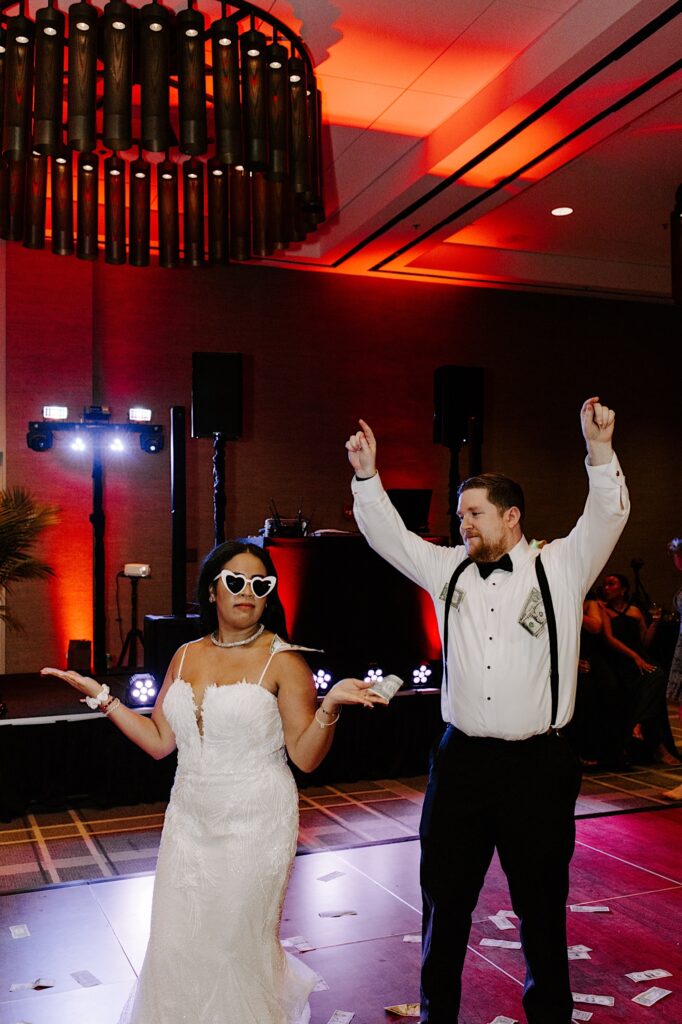 A bride and groom dance together alone on the dancefloor with money all around them during their indoor wedding reception