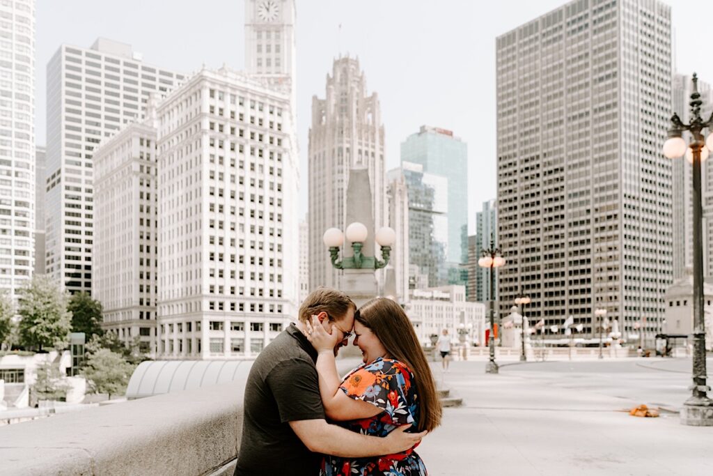 A man and woman embrace and touch their foreheads together while smiling in front of the skyscrapers of Chicago