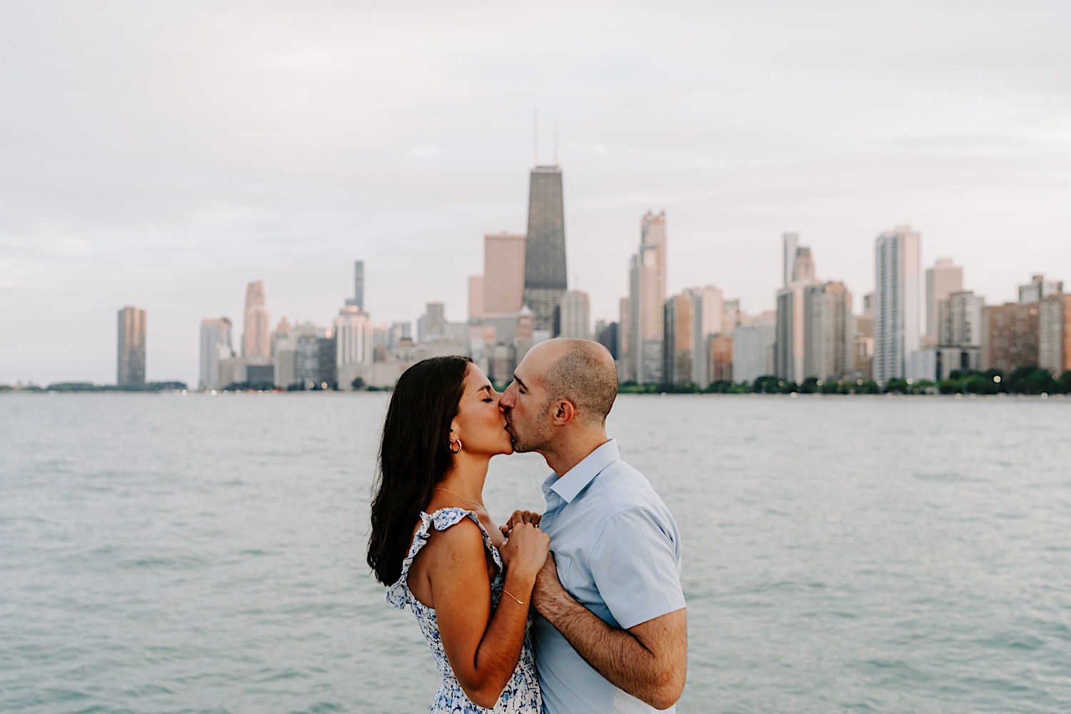 A couple kiss one another with the Chicago skyline and Lake Michigan behind them during their engagement photos