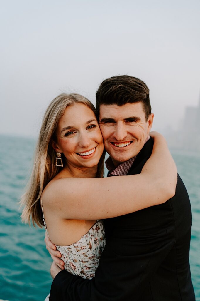 A man and woman smile at the camera while hugging one another with Lake Michigan behind them