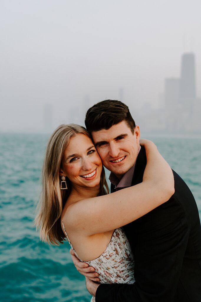 A man and woman smile at the camera while hugging one another with Lake Michigan behind them