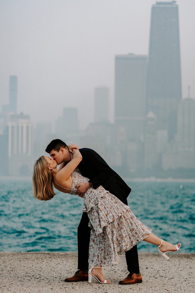 A woman is dipped and kissed by a man in front of Lake Michigan and a hazy Chicago skyline