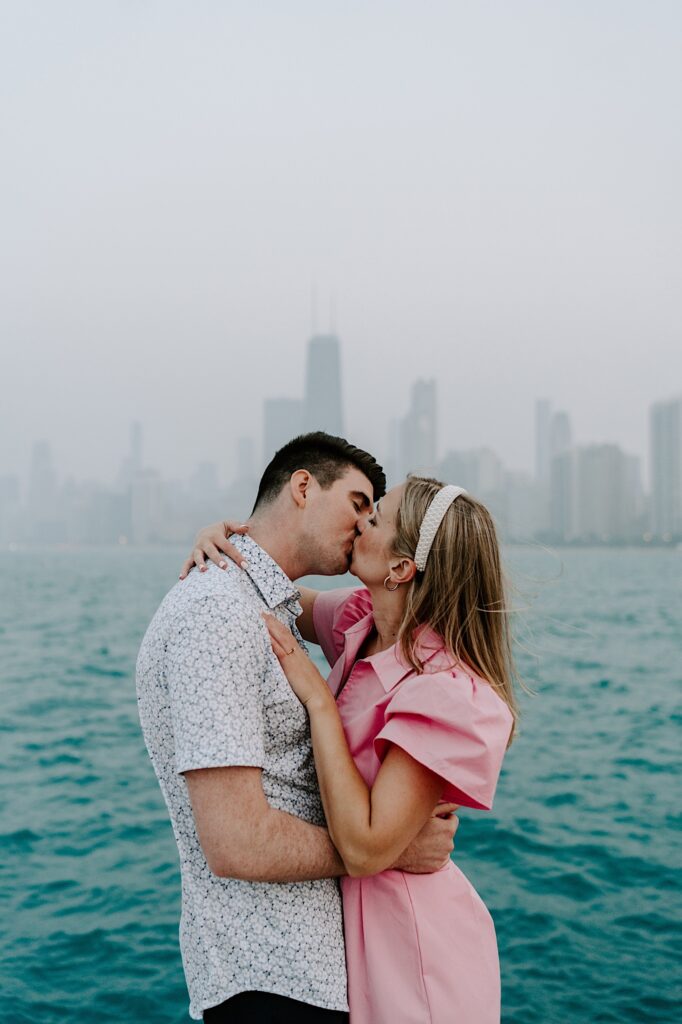 A man and woman kiss one another while embracing in front of Lake Michigan and the Chicago skyline