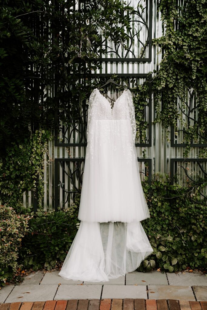 A wedding dress hands on a metal grate with ivy growing on the wall behind it