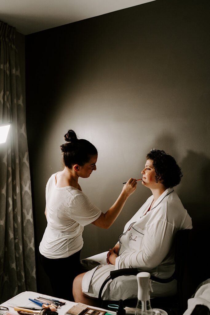 A bride sits in a chair while getting her makeup done before her wedding day