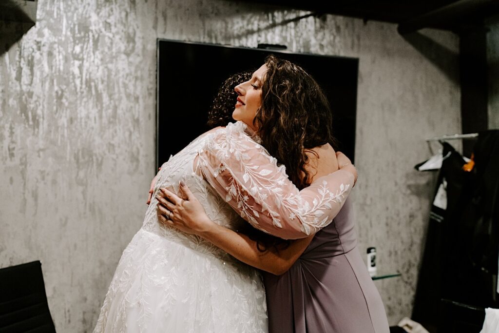 A bride hugs one of her bridesmaids on the day of her wedding after putting her wedding dress on