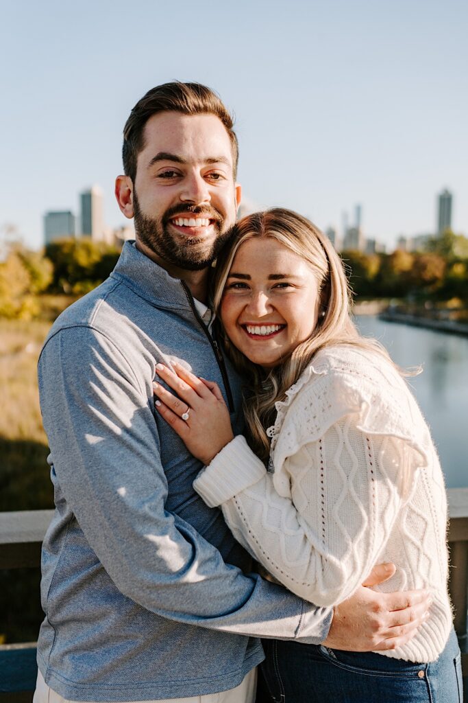 A man and woman embrace one another and smile at the camera while standing on a bridge in Lincoln Park