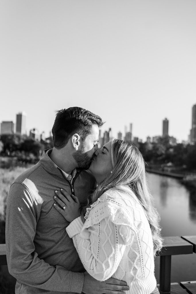 Black and white photo of a man and woman kissing one another while standing on a bridge over a river in Lincoln Park