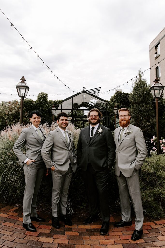 A groom stands and smiles with his three groomsmen while standing outside of their wedding venue