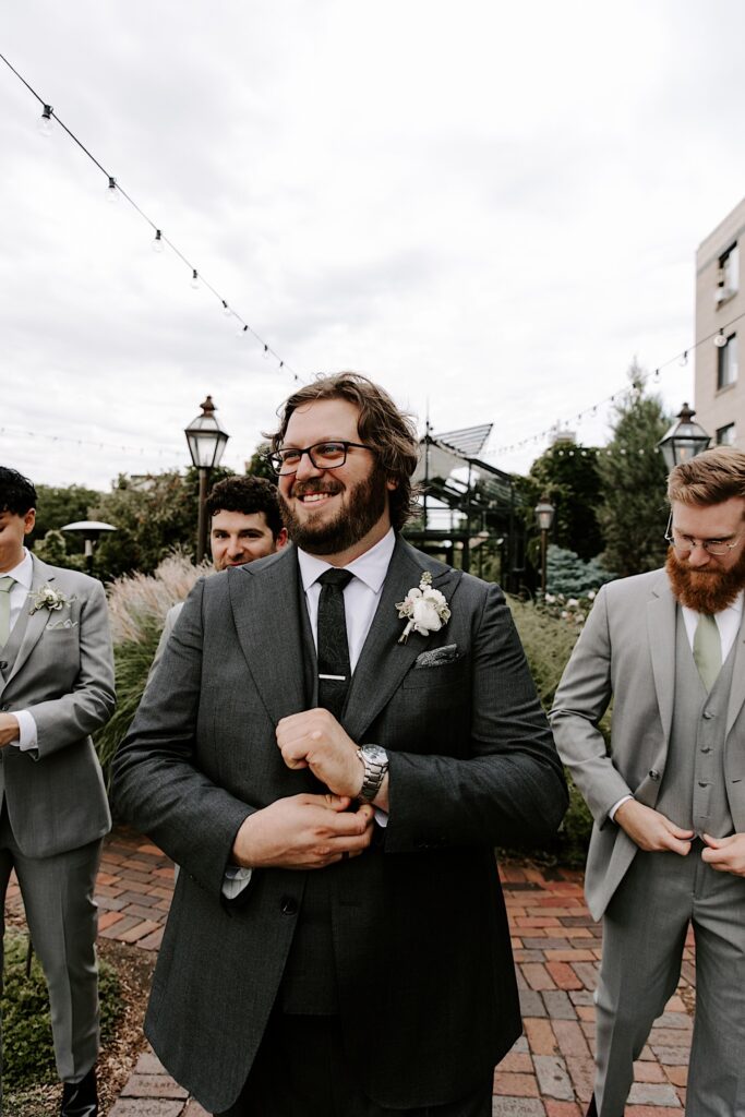 A groom smiles while adjusting the watch on his wrist alongside his three groomsmen