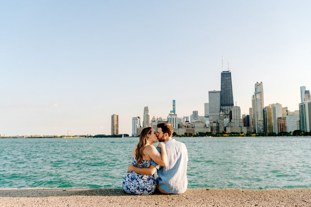 A couple sit at North Avenue Beach together and kiss with Lake Michigan and the Chicago skyline in the background
