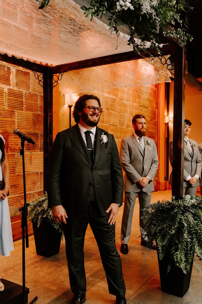 A groom smiles while standing during his wedding ceremony waiting for the bride to enter