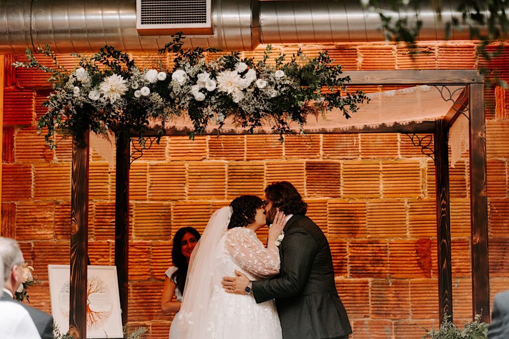 A bride and groom kiss one another in front of a brick wall during their indoor wedding reception at The Atrium in Milwaukee
