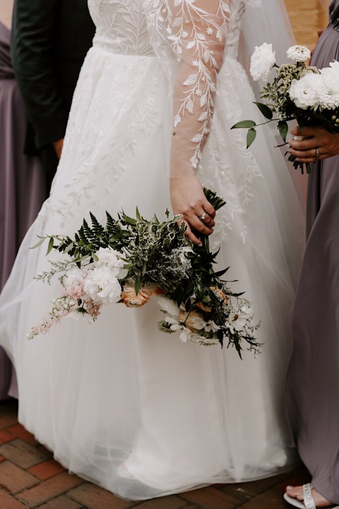 A bride stands holding her flower bouquet at her side