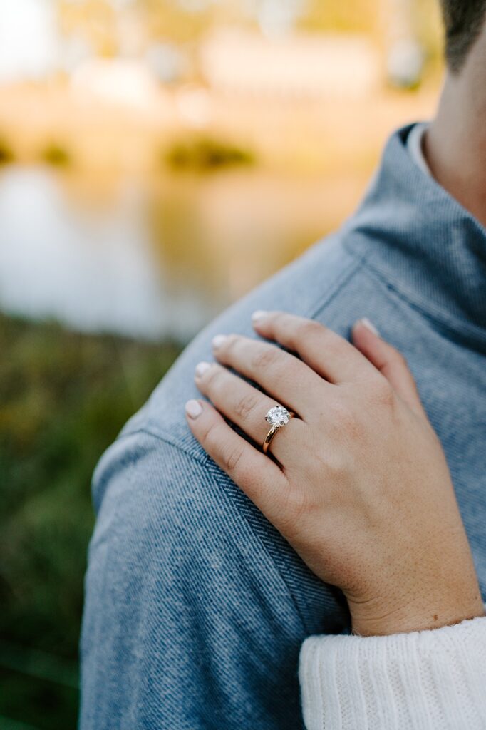 Close up photo of a woman's hand with an engagement ring on it as it rests on the shoulder of a man
