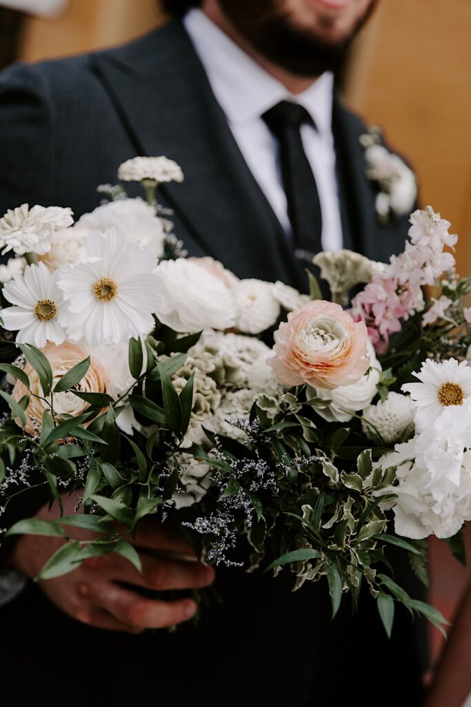 A flower bouquet is held towards the camera by the groom