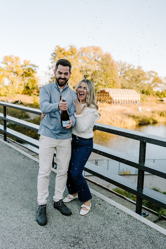 A woman cheers as a man sprays a bottle of champagne in the air to celebrate their engagement as they stand on a bridge in Lincoln Park of Chicago