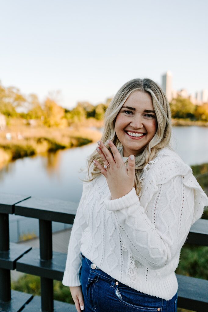 A woman smiles at the camera while showing off her engagement ring as she stands on a bridge in Lincoln Park of Chicago