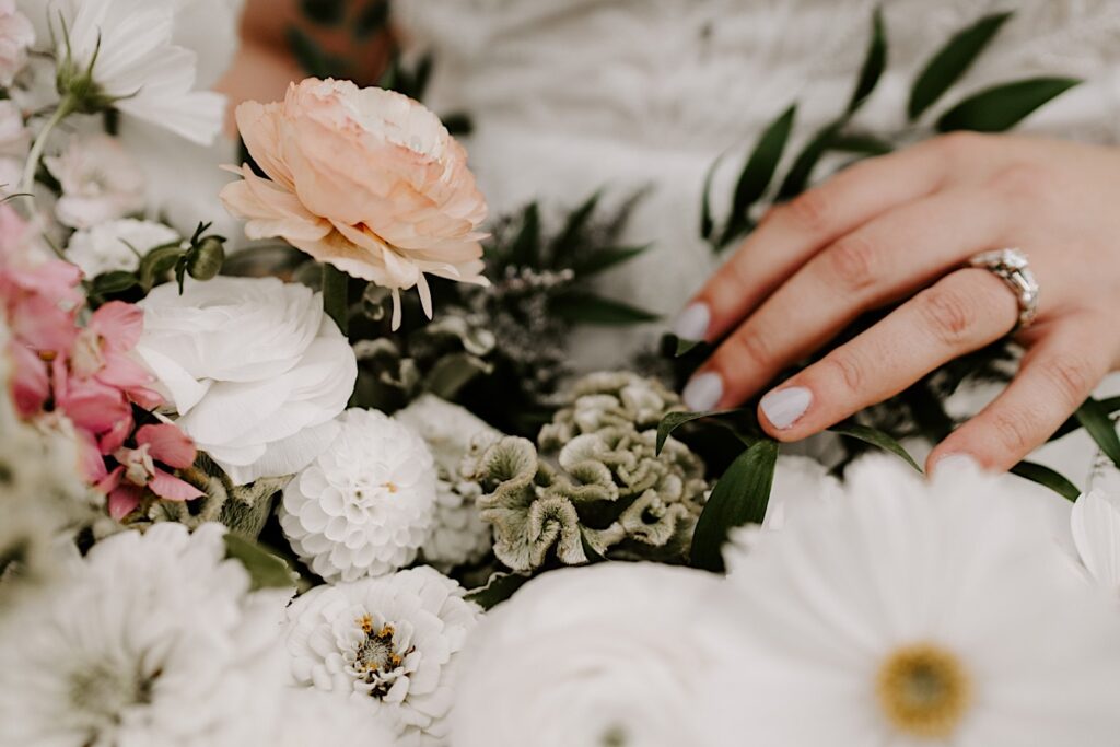 Close up photo of the bride's hand with her wedding ring on resting next to a flower bouquet