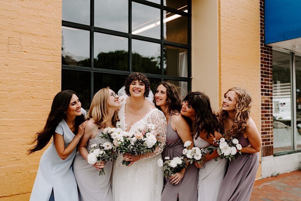 A bride smiles with her 5 bridesmaids while they stand outside of the wedding venue The Atrium in Milwaukee