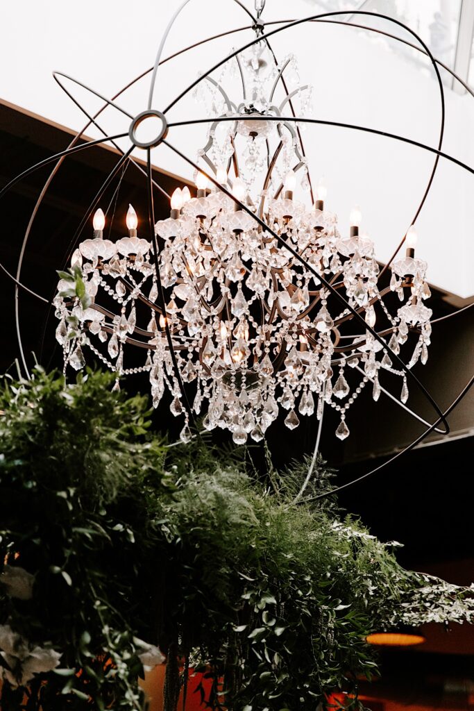 A large glass chandelier hangs under a skylight in a wedding venue